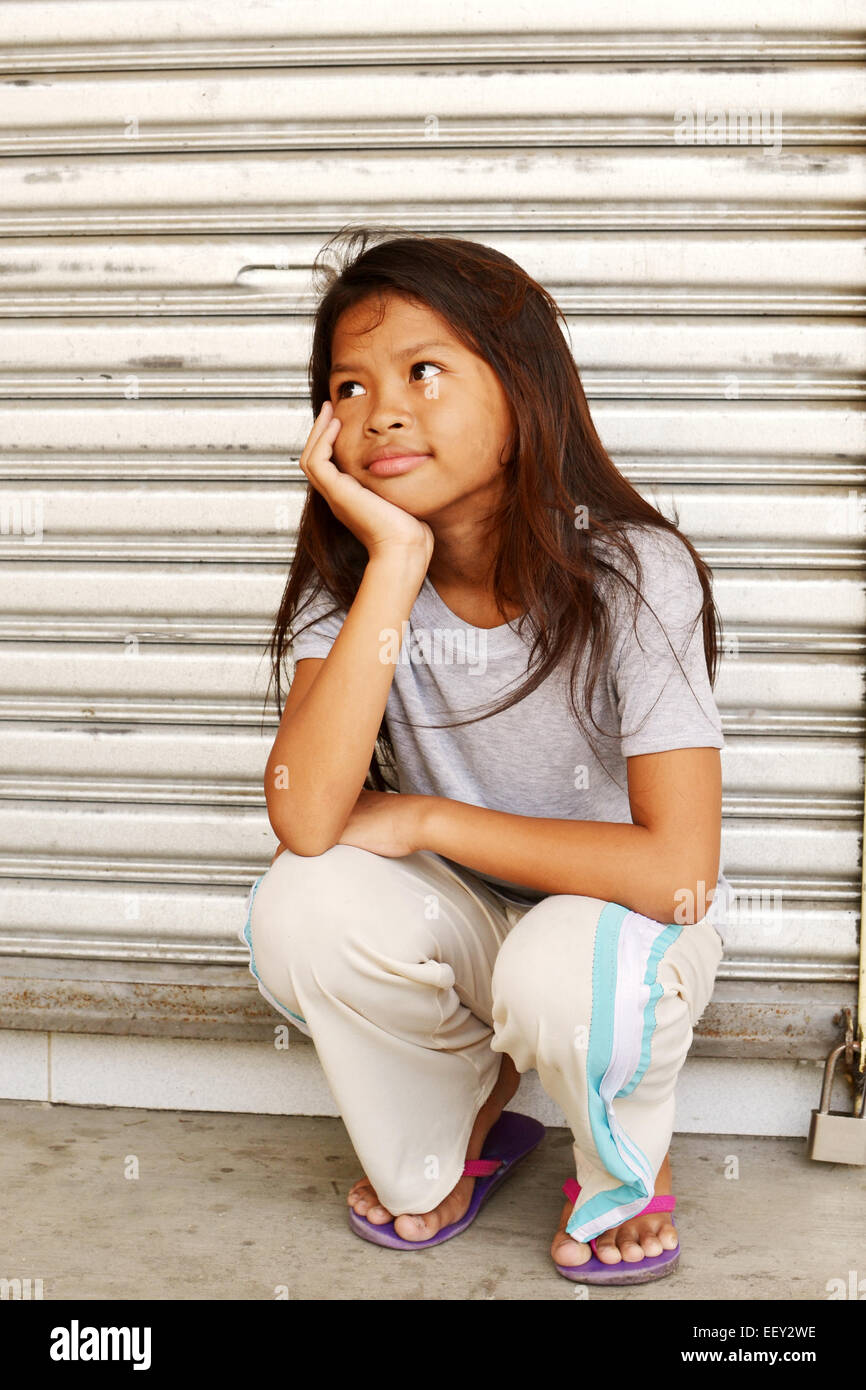 Homeless poor girl sitting on the sidewalk watching something with a smile Stock Photo