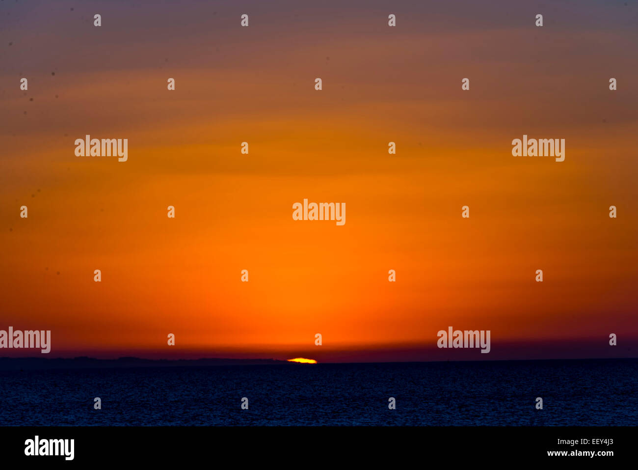 Sunset over sea ocean bright orange blue sky moody dusk Stock Photo