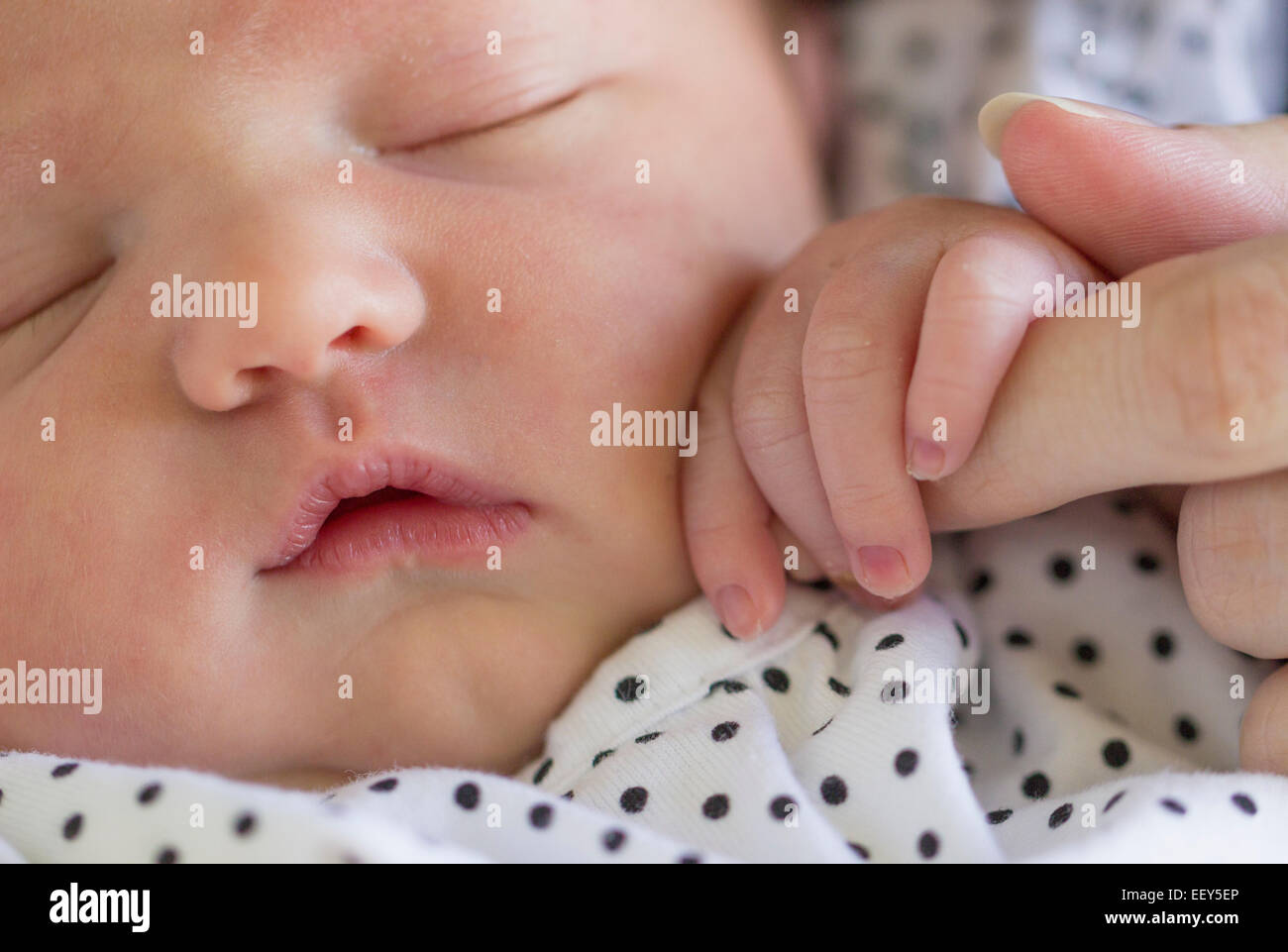 Newborn baby girl asleep and gripping the finger of her mother close to her face Stock Photo