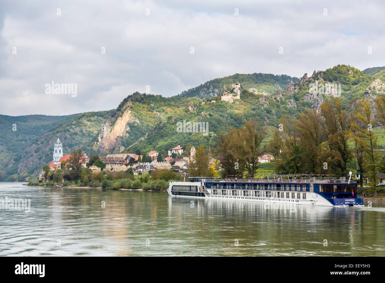 River cruise tour boat on River Danube approaches the ancient town and church in Durnstein, Austria Stock Photo