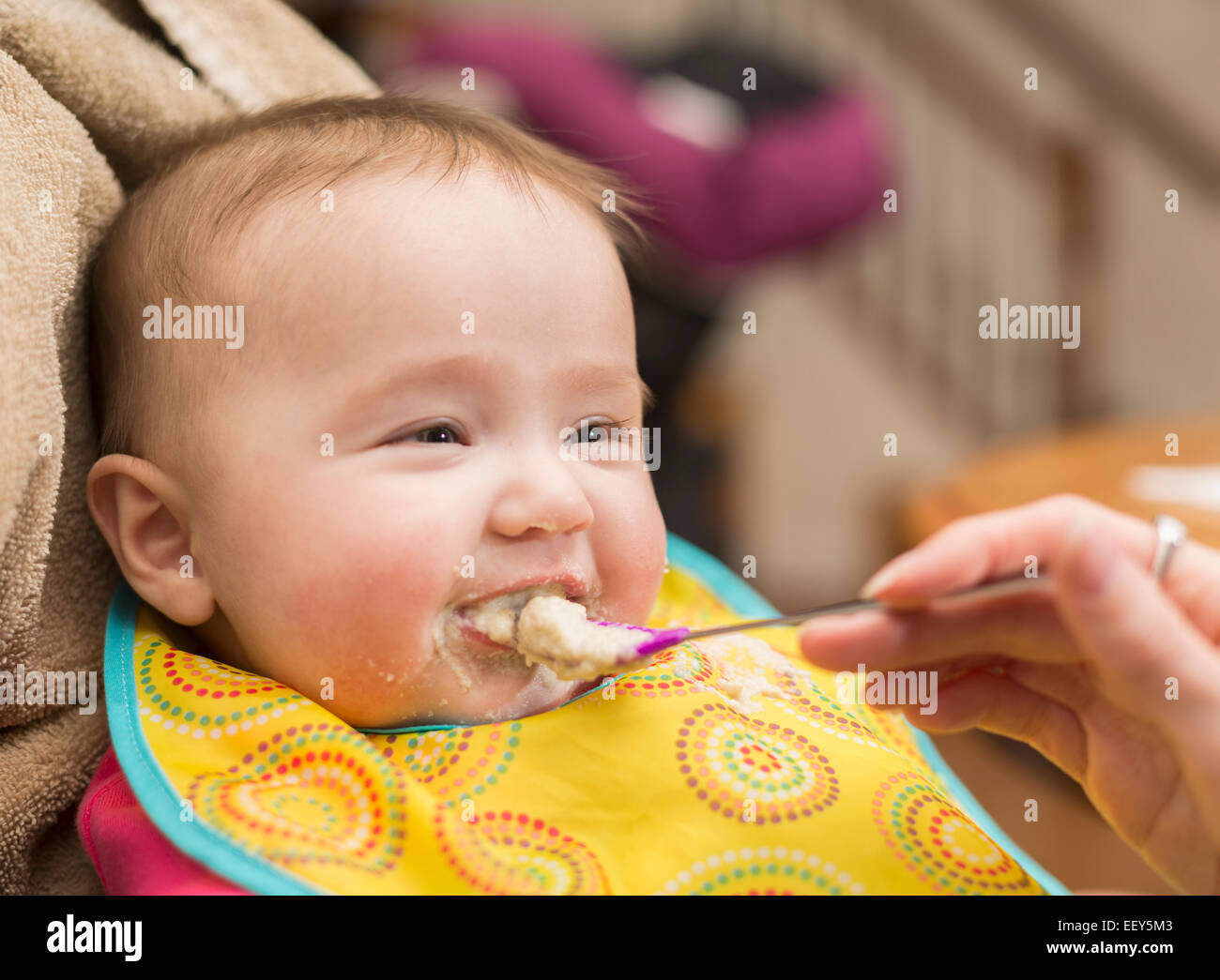 Small baby girl is given her first solid food on a spoon and is unsure about the process Stock Photo
