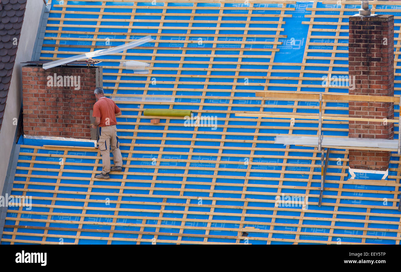 Builder on a steep roof on building without any safety equipment Stock Photo