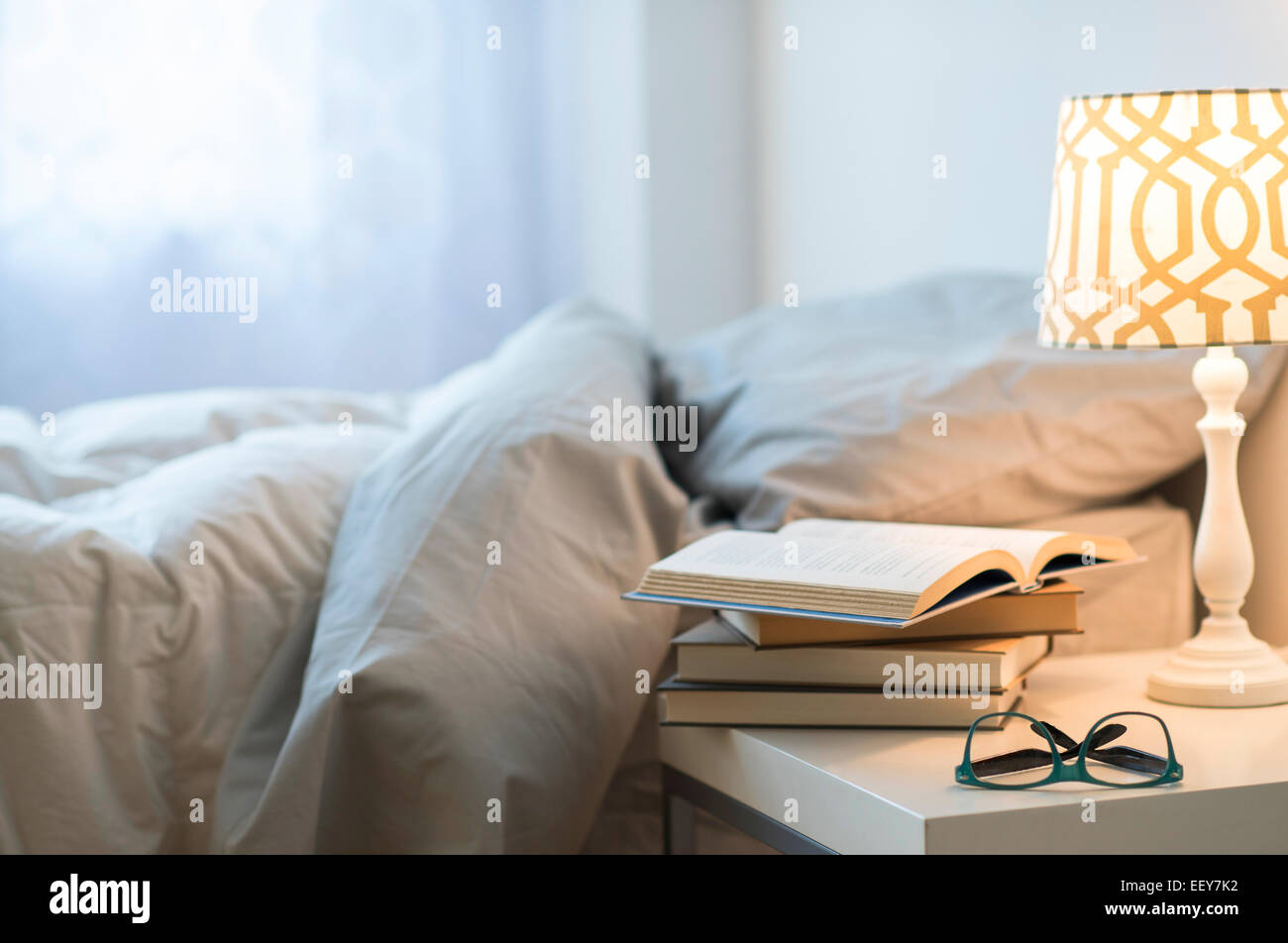 Bed with lamp, books and glasses on bedside table Stock Photo