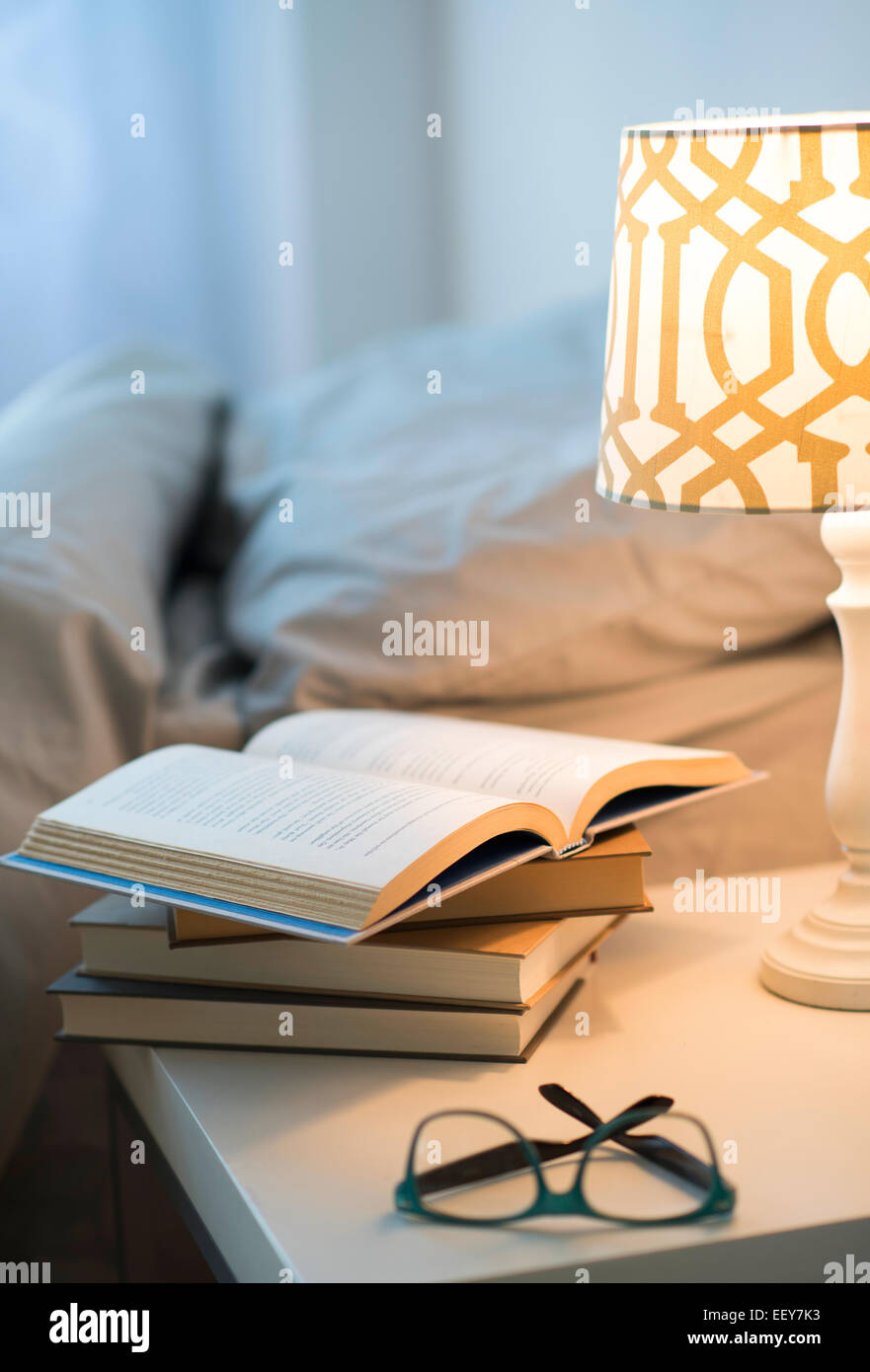 Bed with lamp, books and glasses on bedside table Stock Photo