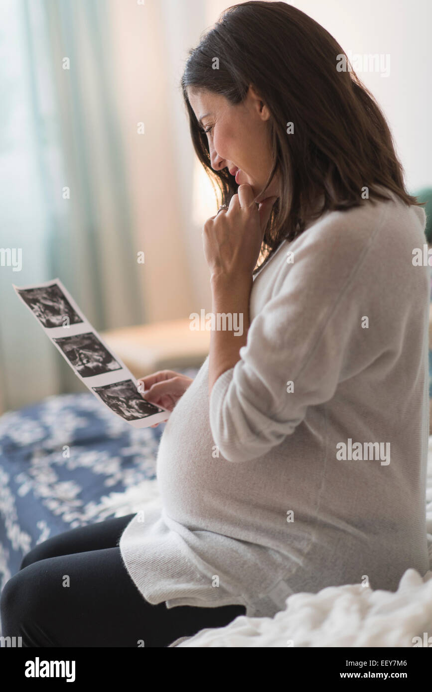 Pregnant woman watching ultrasound, sitting on bed Stock Photo