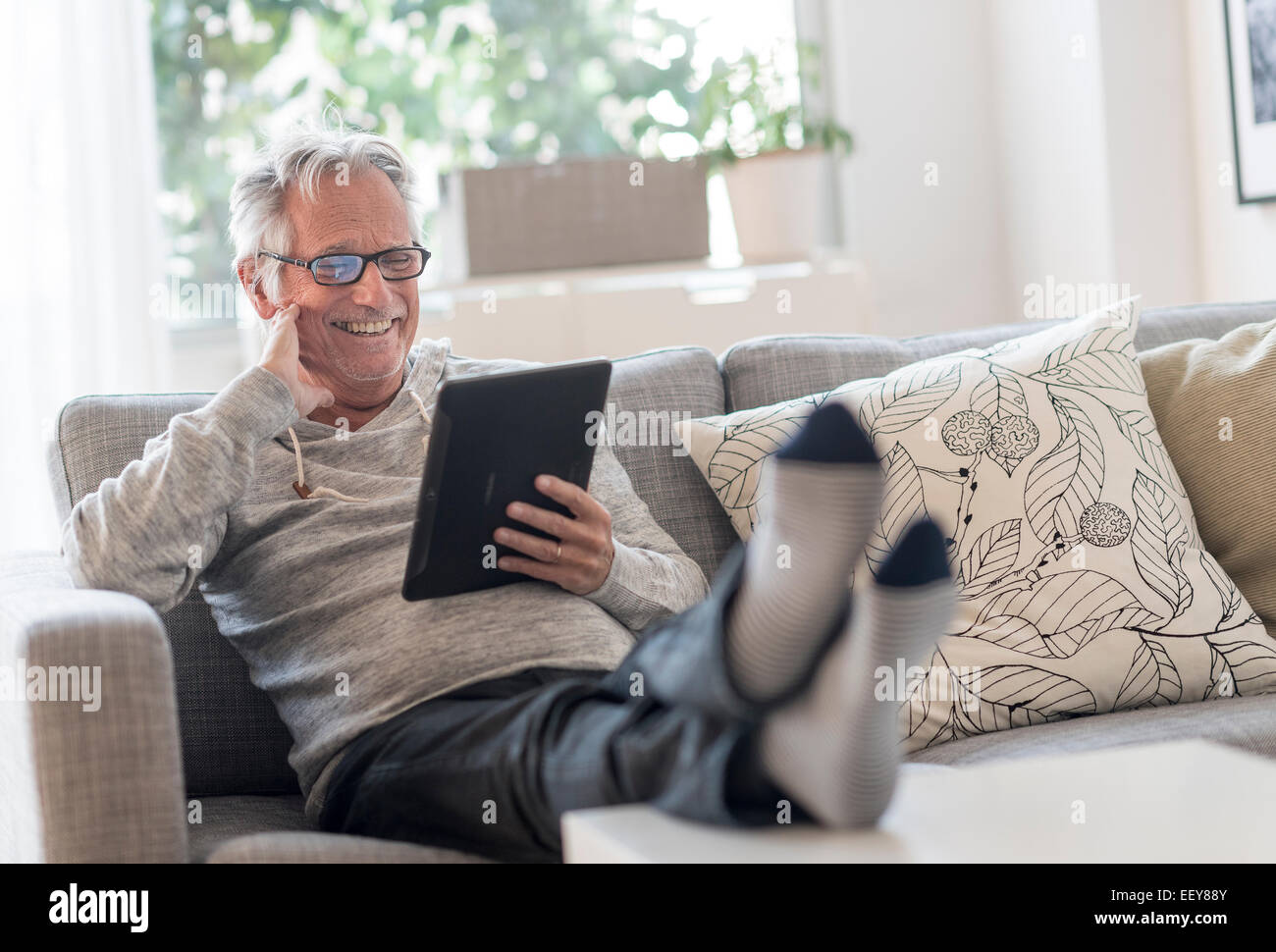 Senior man sitting on couch in living room, using tablet pc and smiling Stock Photo