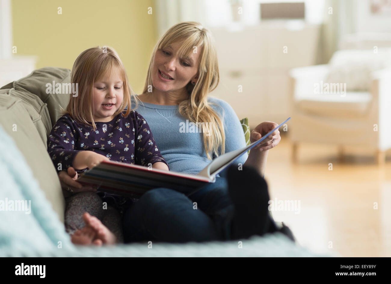 Mother and daughter (4-5) sitting on couch and reading book Stock Photo