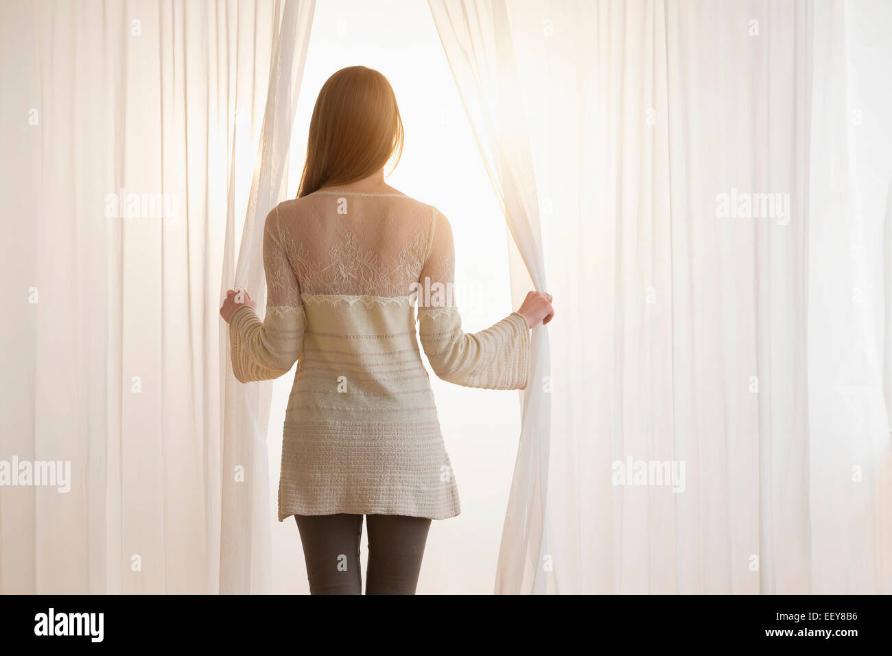 Young woman opening curtains in morning Stock Photo