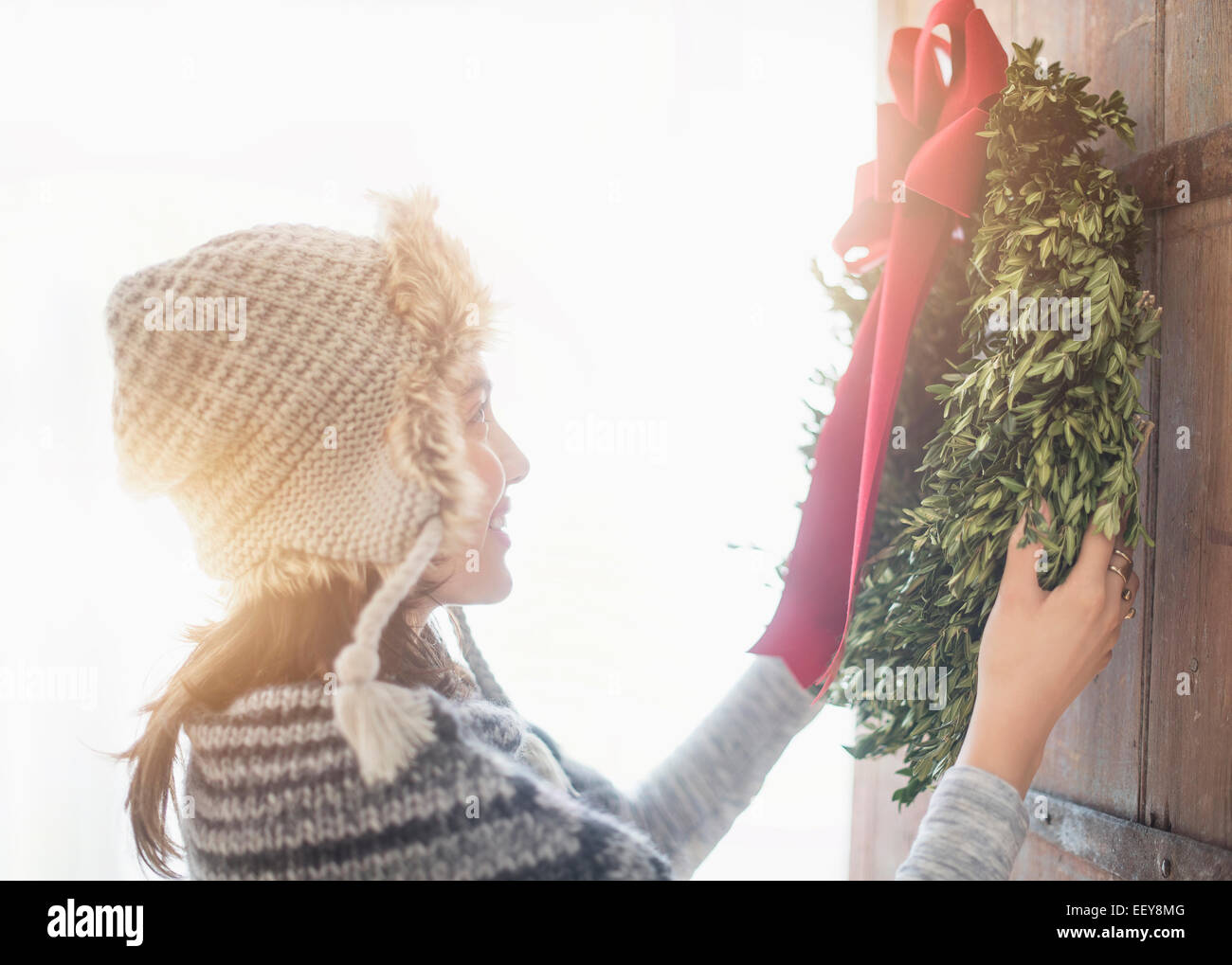 Side view of young woman hanging Christmas wreath on entrance door Stock Photo