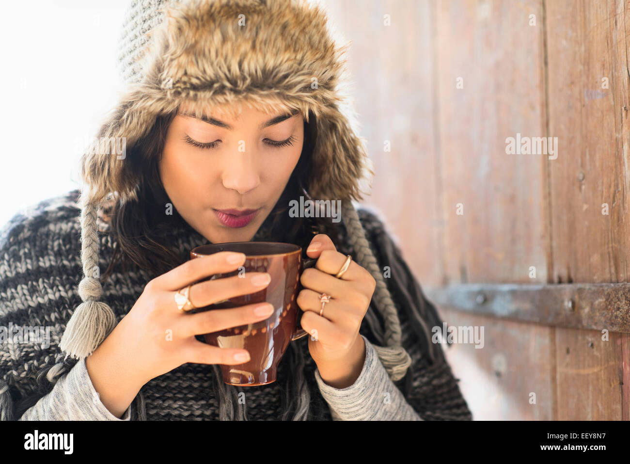 Portrait of young woman wearing warm hat, blowing on cup of drink Stock Photo