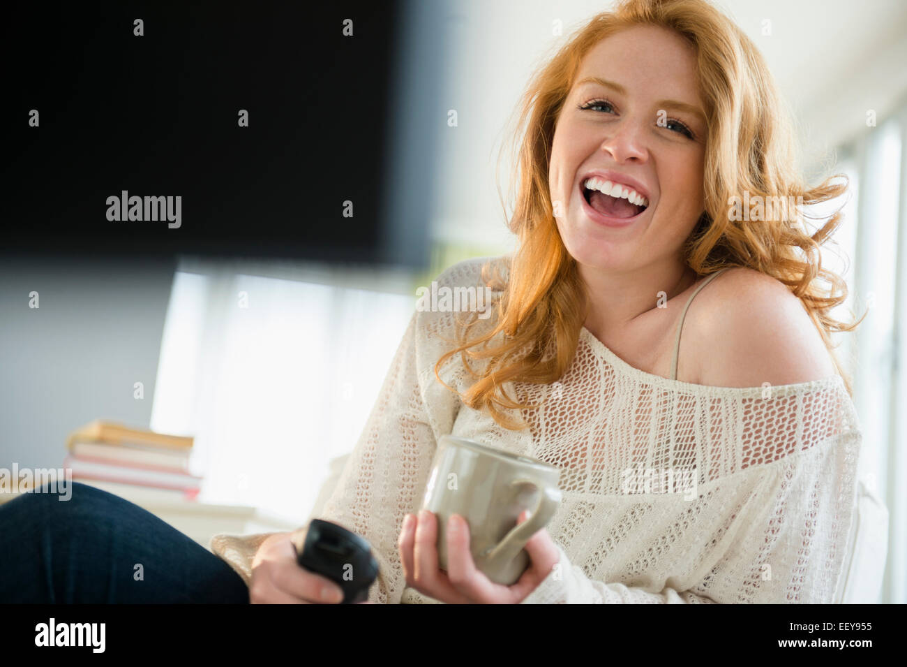 Young woman watching television and laughing Stock Photo