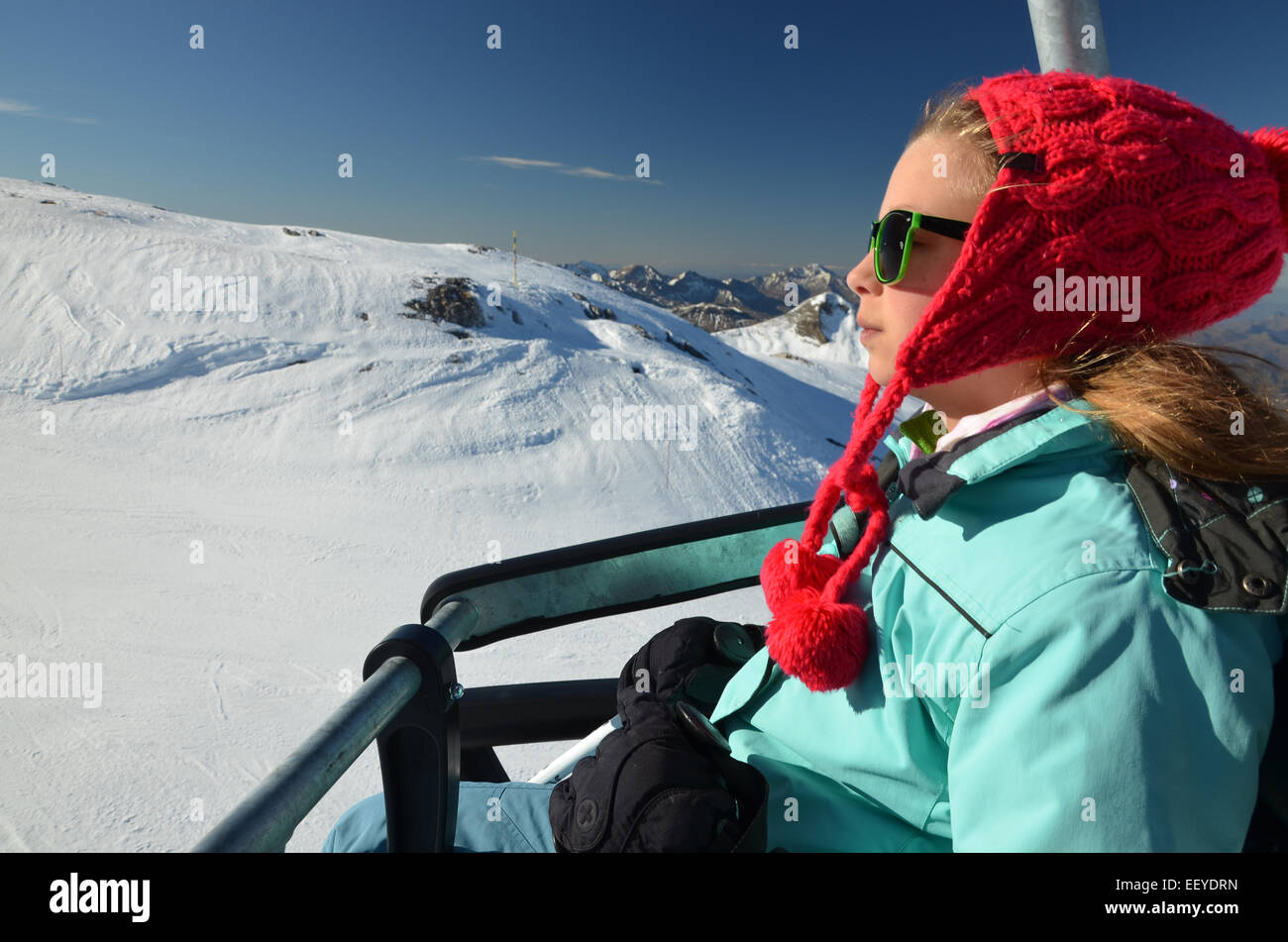Young girl with red winter hat and  sun glasses on  chair lift at ski resort Pierre saint martin in Atlantic Pyrenees, white sno Stock Photo