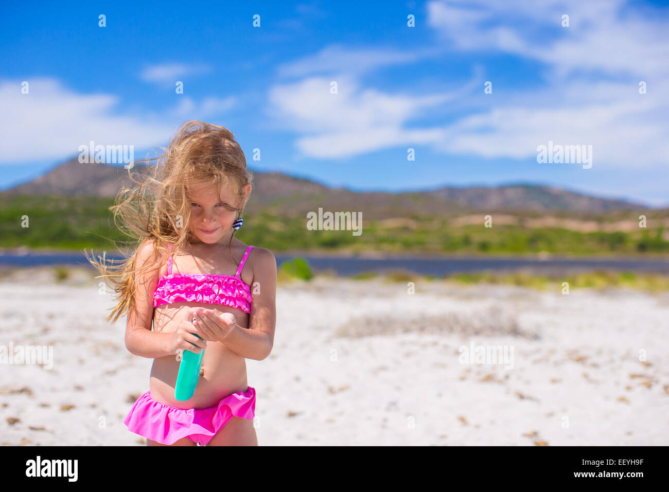 Little adorable girl in swimsuit with suntan lotion bottle Stock Photo