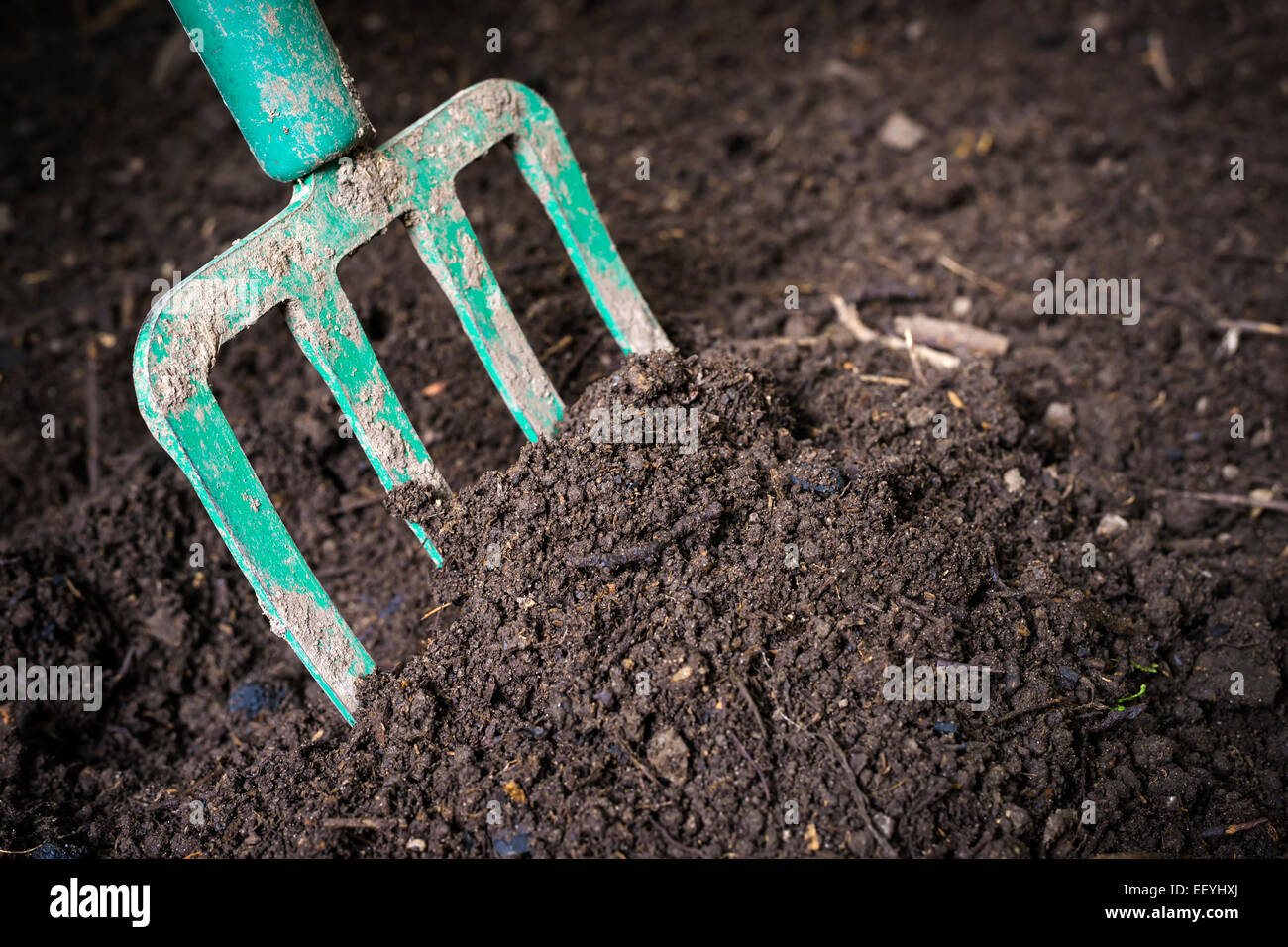 Garden fork turning black composted soil in compost bin ready for