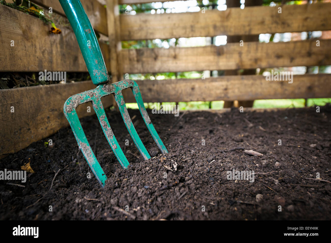 Garden fork turning black composted soil in wooden compost bin Stock Photo