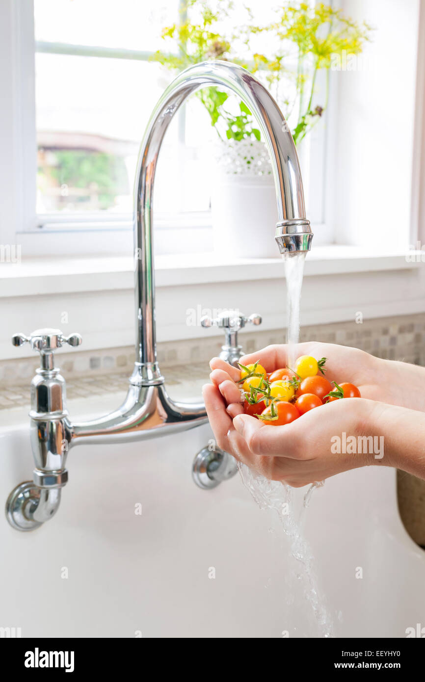 Hands washing fresh cherry tomatoes in running water of kitchen sink with curved faucet Stock Photo