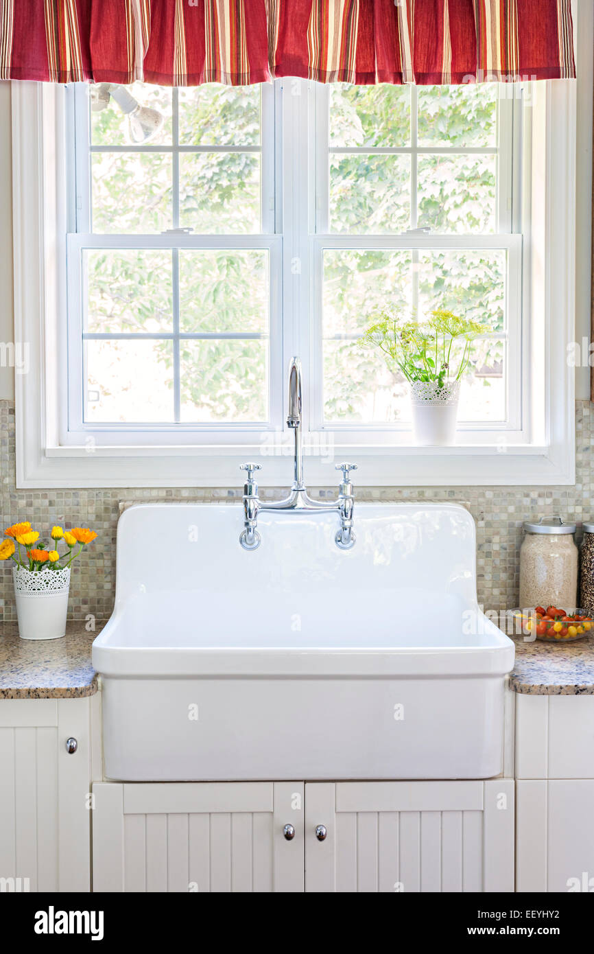 Kitchen interior with large rustic white porcelain sink and granite stone countertop under sunny window Stock Photo