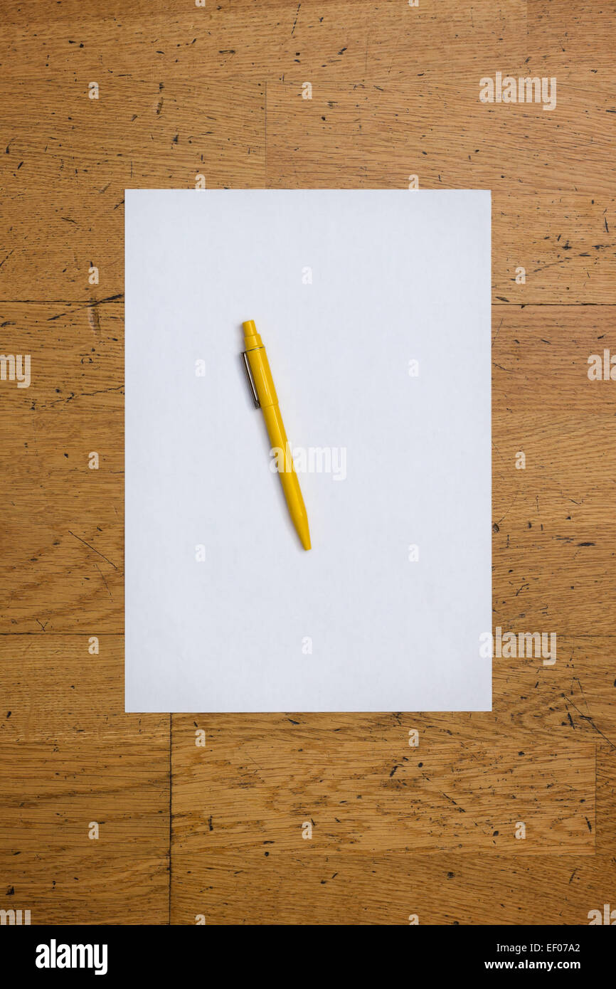 Pen on a blank white paper sheet on a worn wooden table surface, viewed from above Stock Photo
