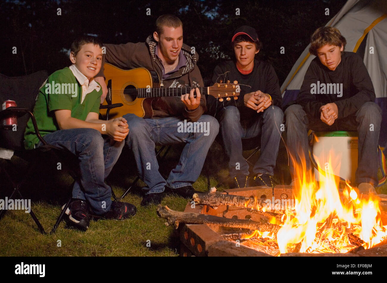 Four teenage boys sitting by campfire Stock Photo