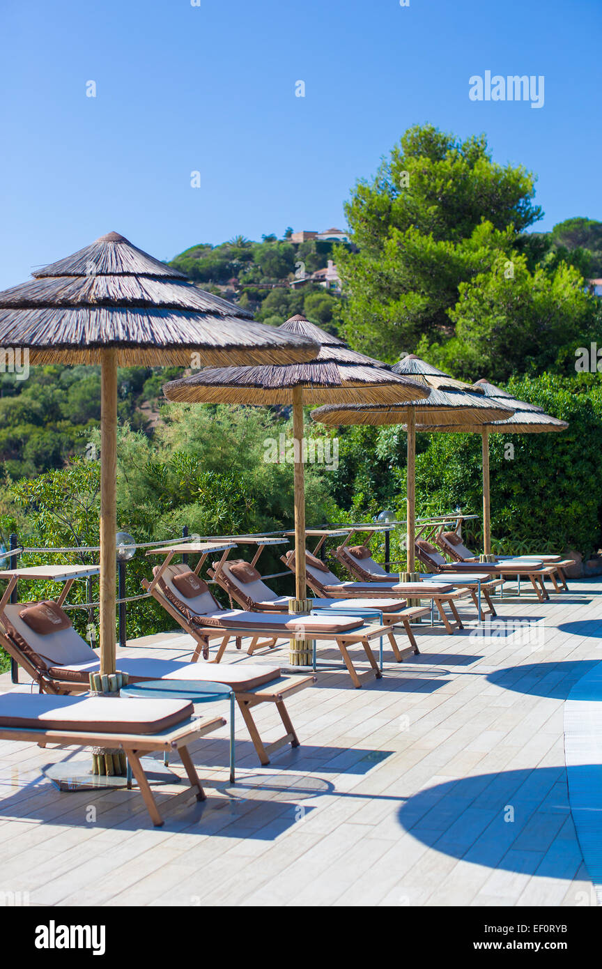 Wooden deck chairs and umbrellas near infinity pool in luxury resort
