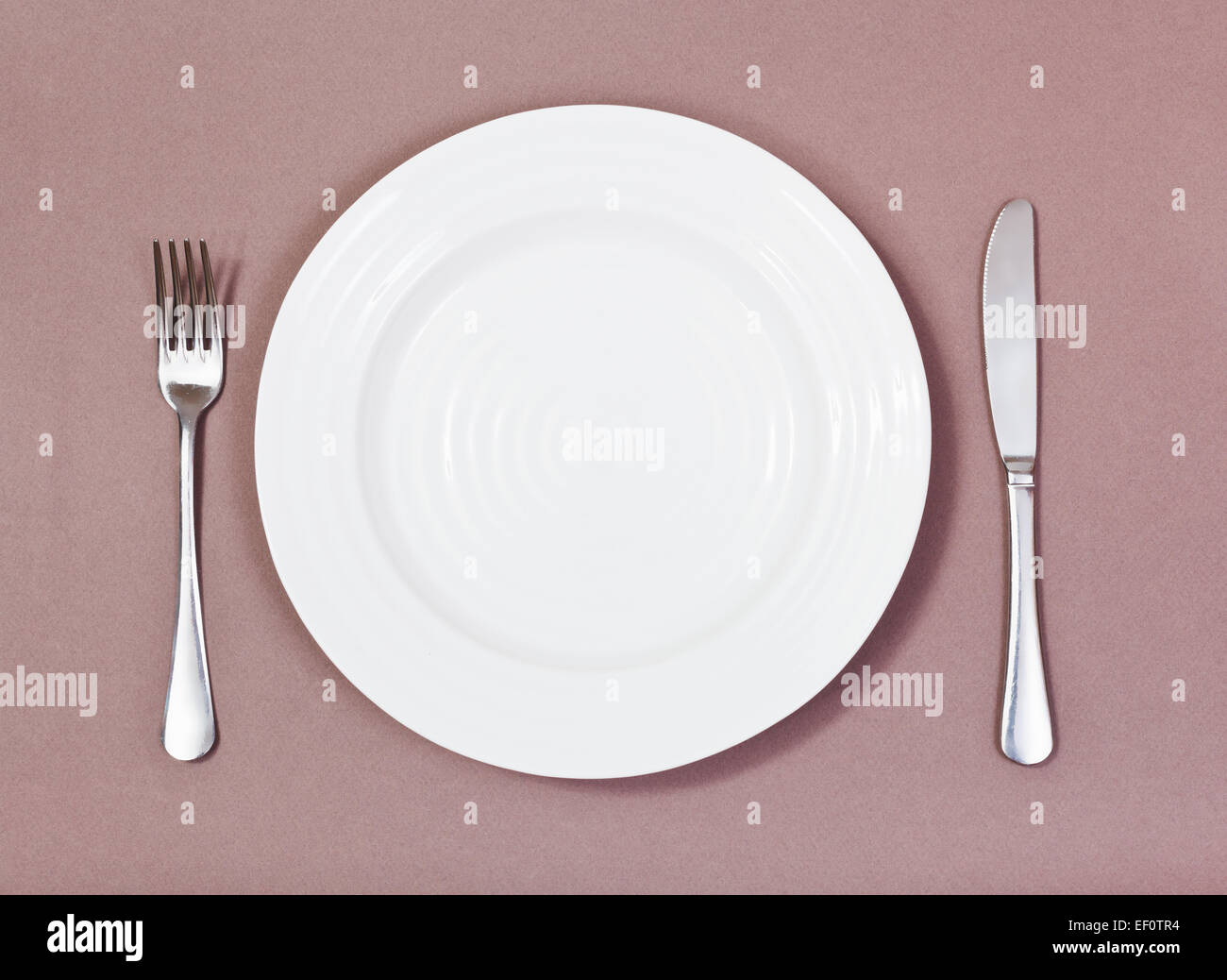 top view of empty white plate with fork and knife on brown background ...