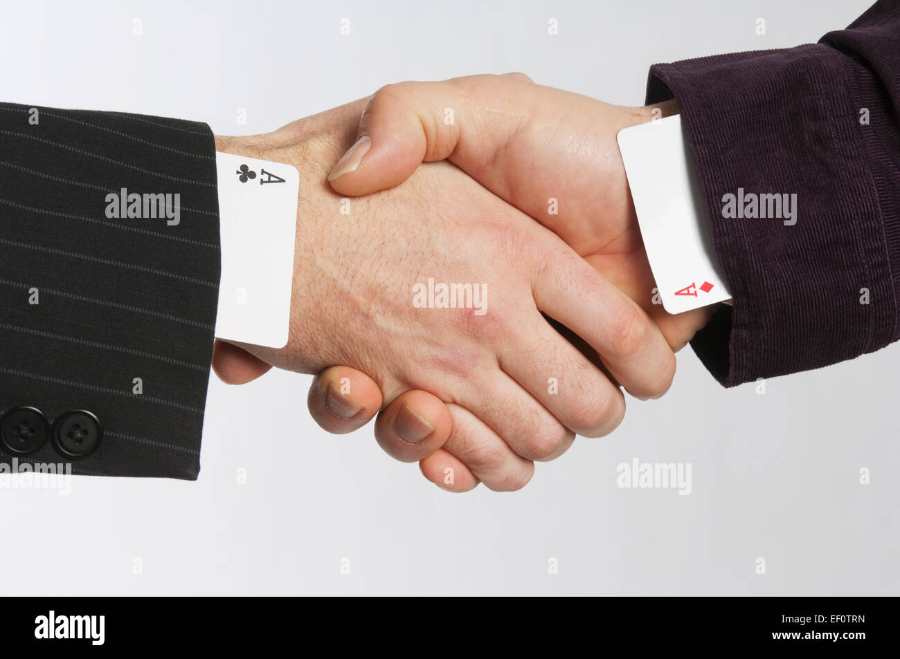 Businessmen shaking hands with cards up their sleeves Stock Photo