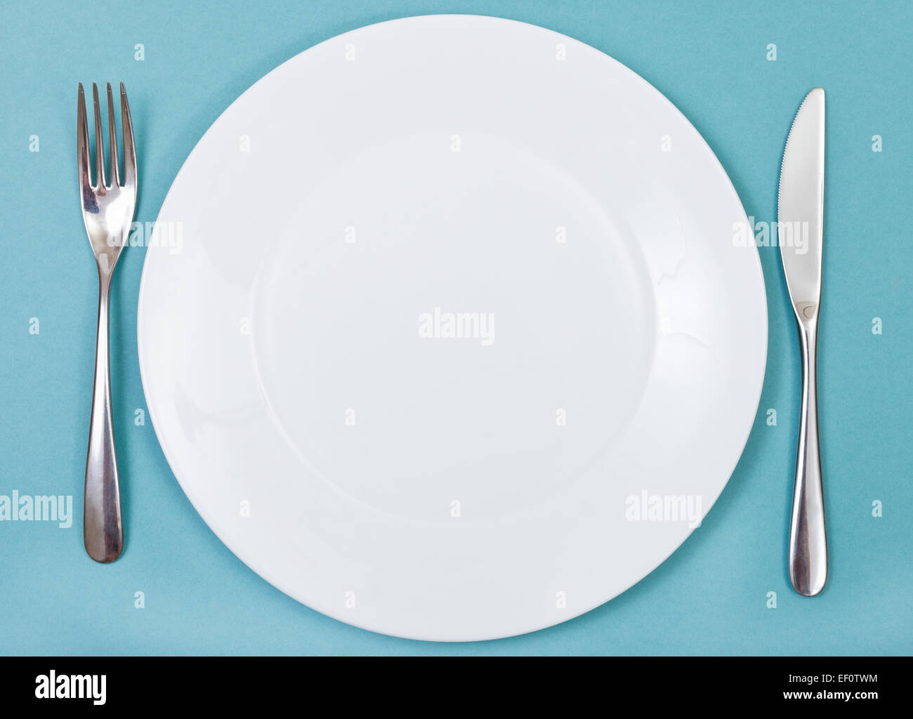top view of empty white porcelain plate with fork and knife set on ...