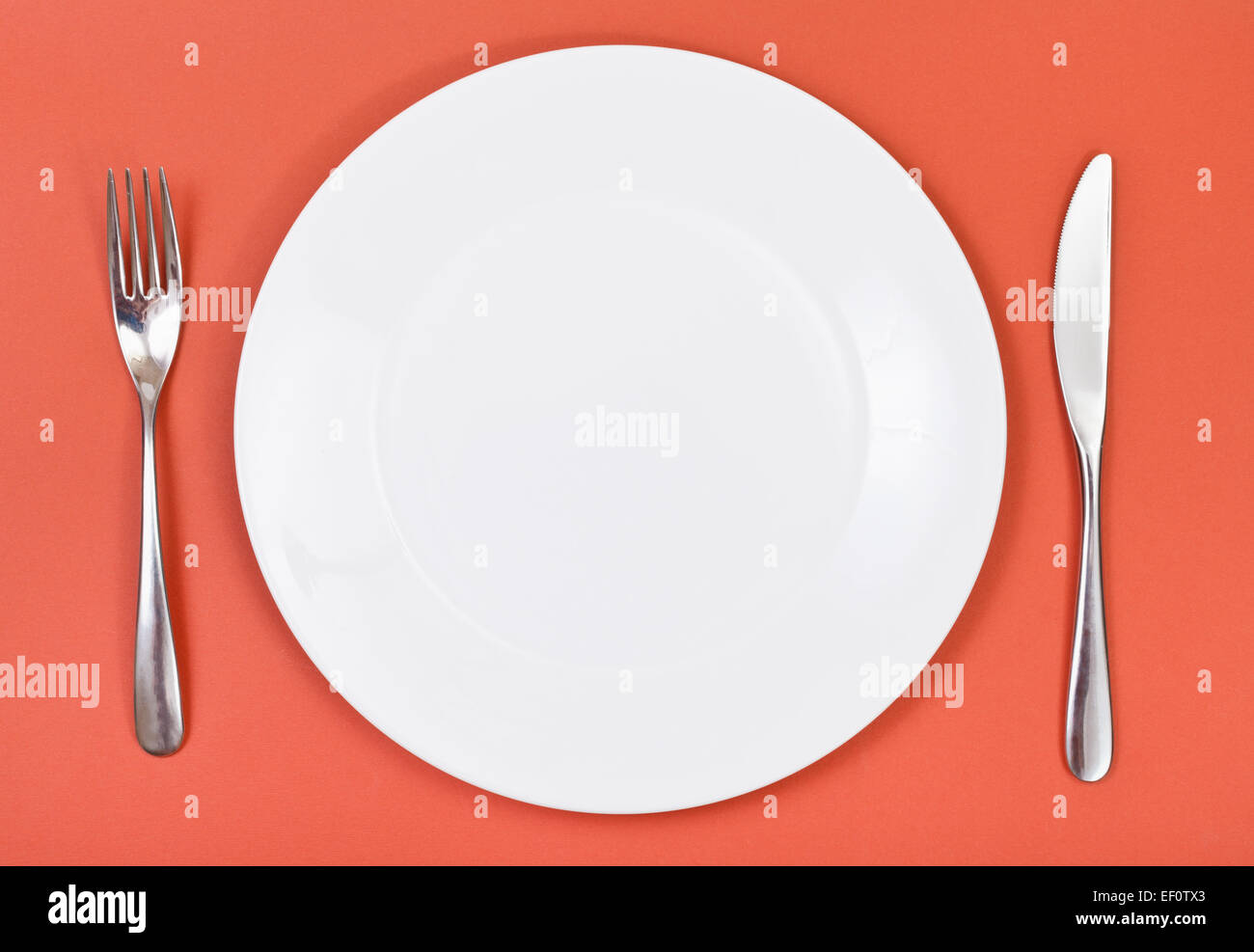 top view of empty white porcelain plate with fork and knife set on red ...