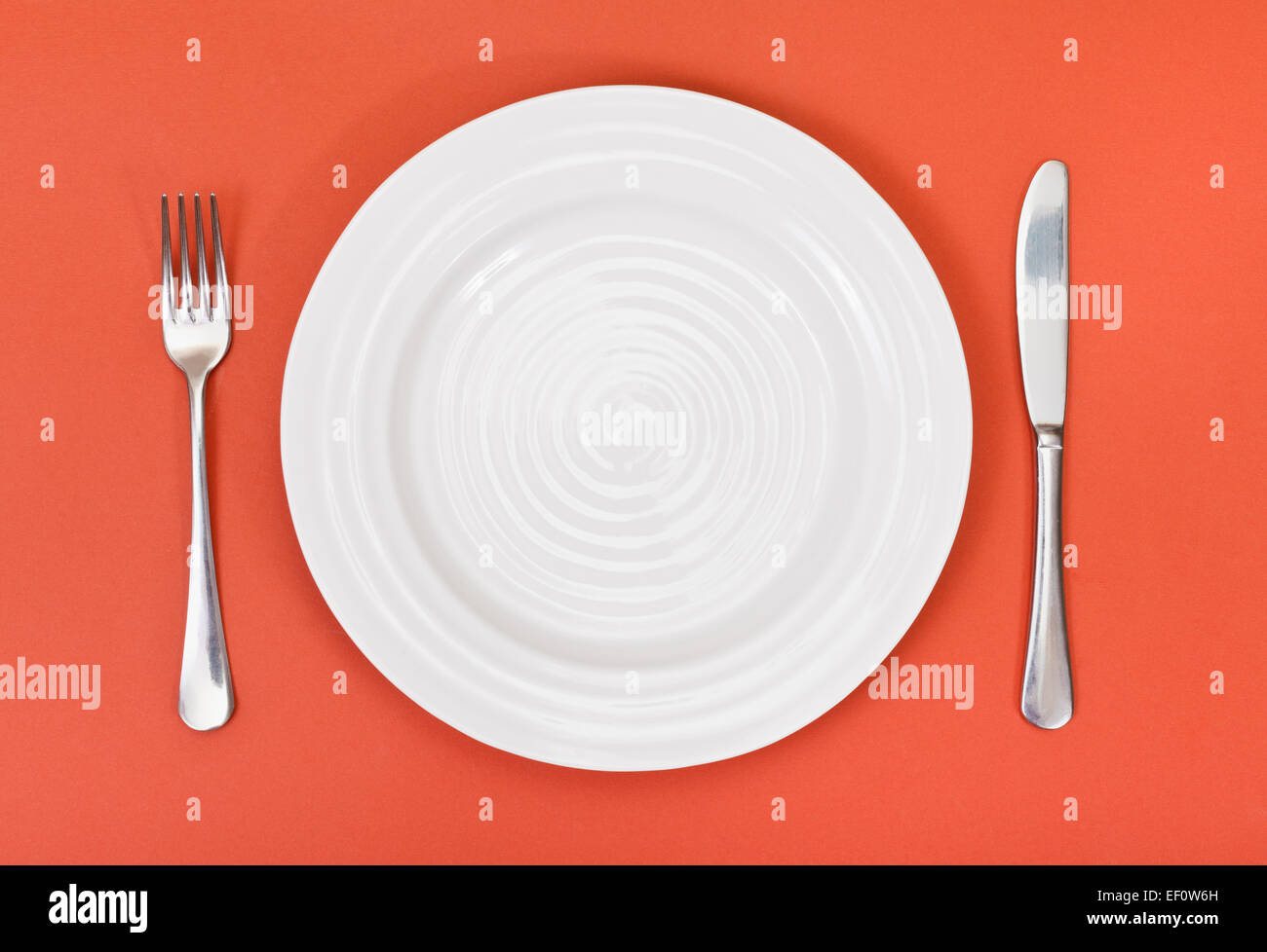 top view of empty white plate with fork and knife set on red background ...