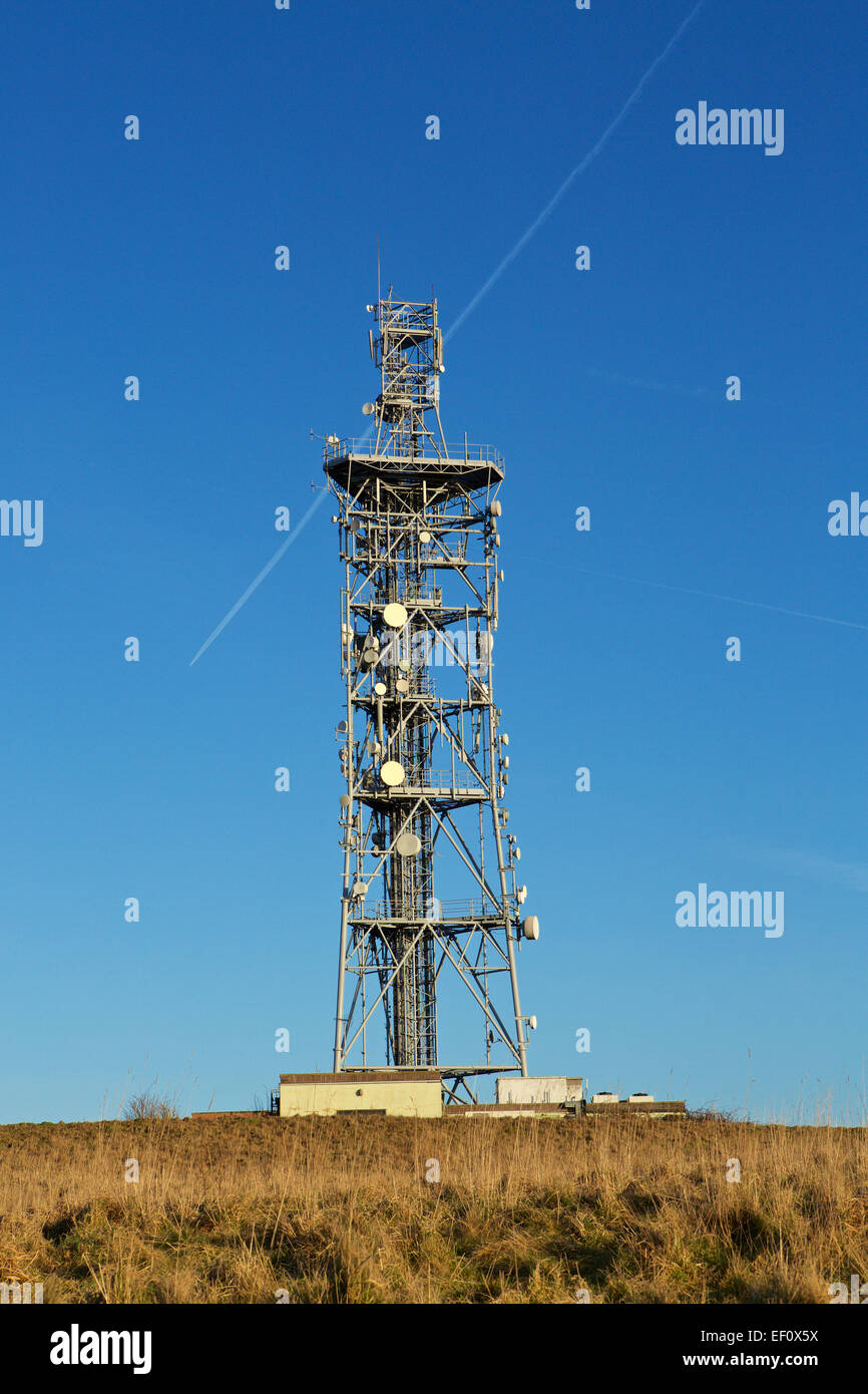 Telecommunications Tower. Full ladened radio mast against a blue sky. Contrail passing behind. Stock Photo