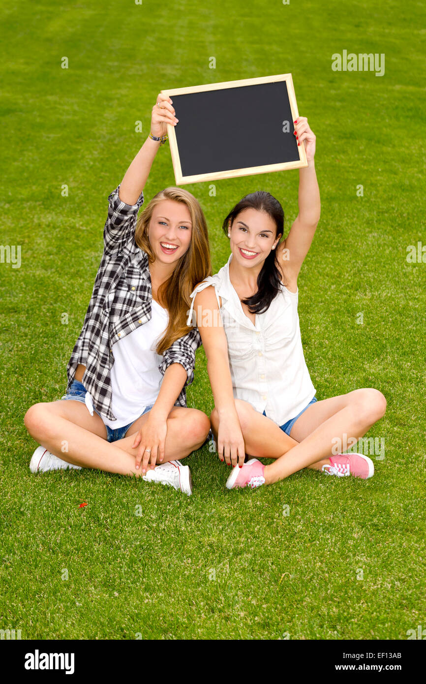 Tennage students sitting on the grass and holding a chalkboard Stock Photo