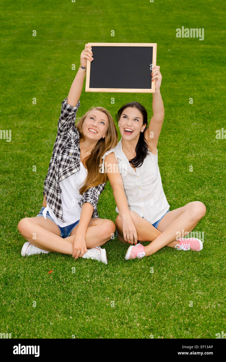 Tennage students sitting on the grass and holding a chalkboard Stock Photo