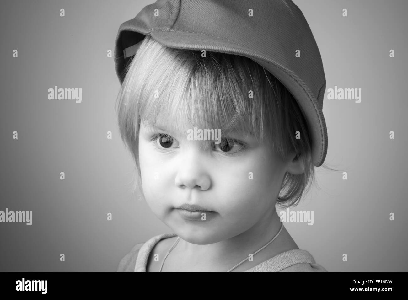 Black and white studio portrait of serious Caucasian baby girl in big baseball cap Stock Photo