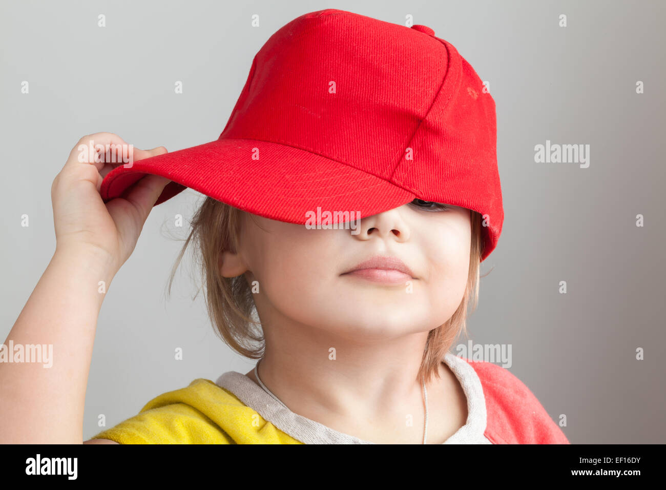Studio portrait of funny baby girl in red baseball cap over gray wall background Stock Photo