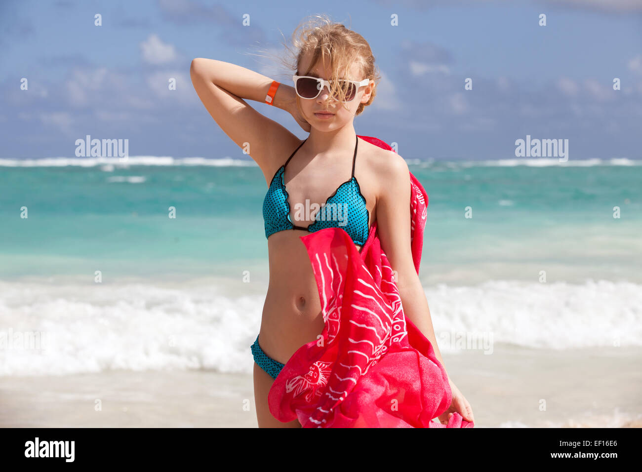 Outdoor portrait of beautiful Caucasian teen girl in blue swimsuit and red shawl standing on the ocean coast Stock Photo