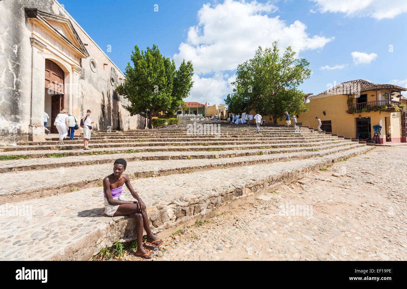 Cuban lifestyle: Very thin local Cuban young woman sitting on steps in downtown Trinidad, Cuba on a sunny day with a blue sky and white clouds Stock Photo