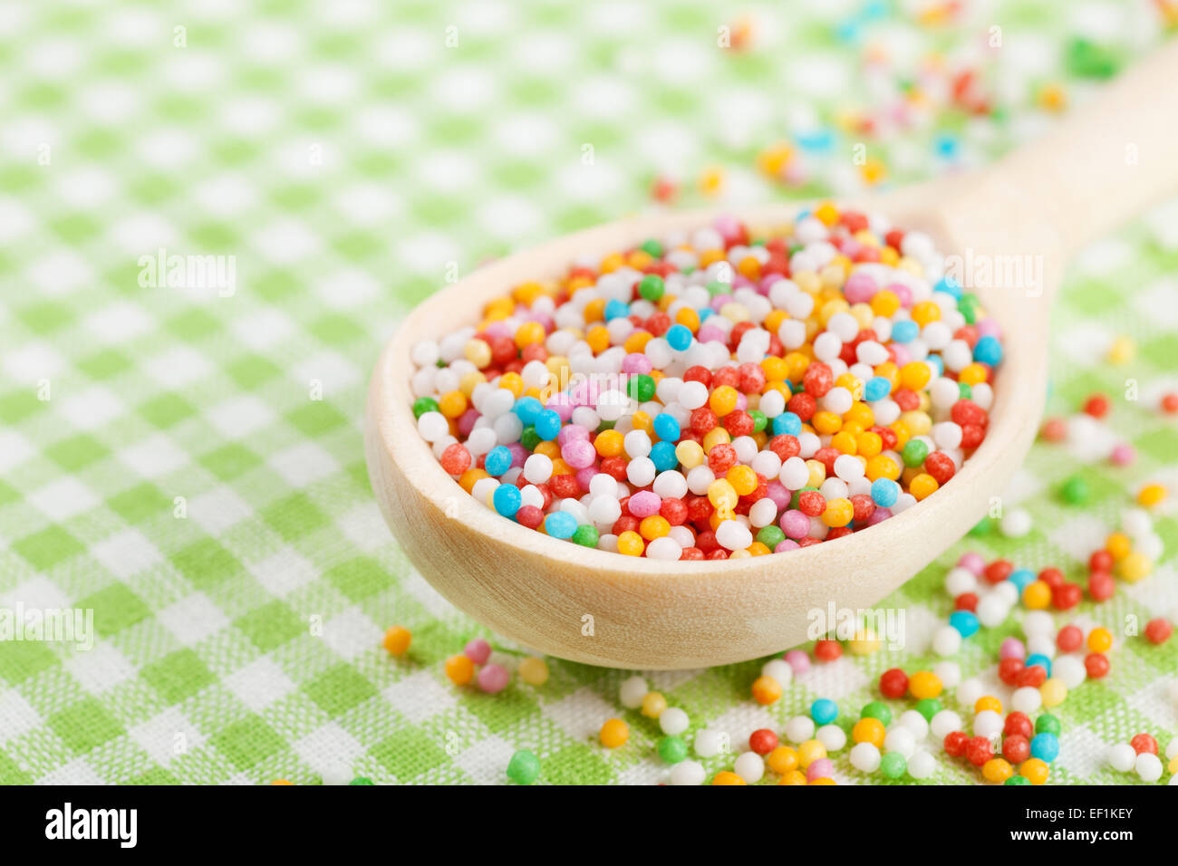 colorful sugar sprinkles in wooden spoon on tablecloth Stock Photo