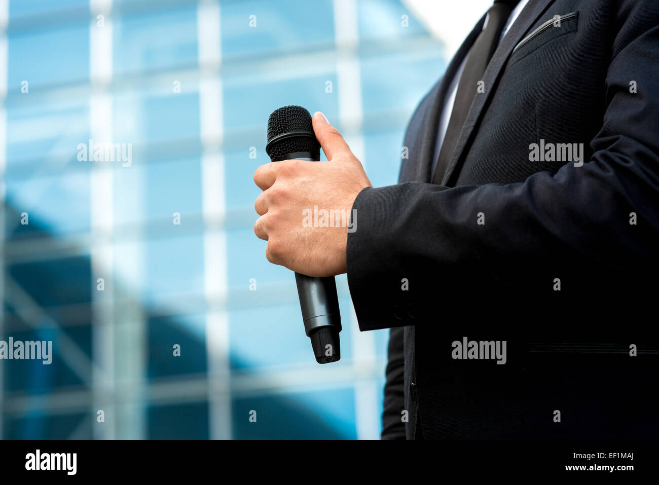 Man holding microphone in the hand on blue contempopary background Stock Photo