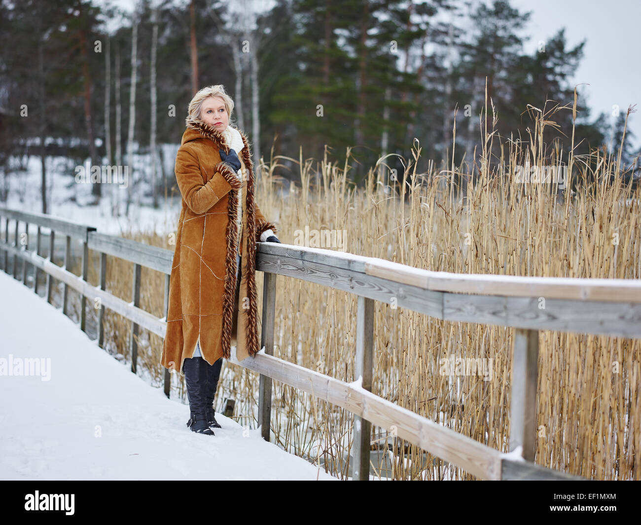 Fashionable mature adult woman wearing winter clothes and she standing next to the fence - rural scene Stock Photo