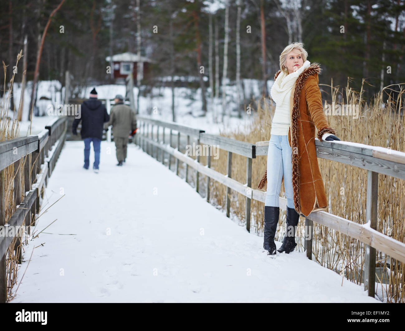 Fashionable mature adult woman wearing winter clothes and she standing next to the fence - rural scene Stock Photo