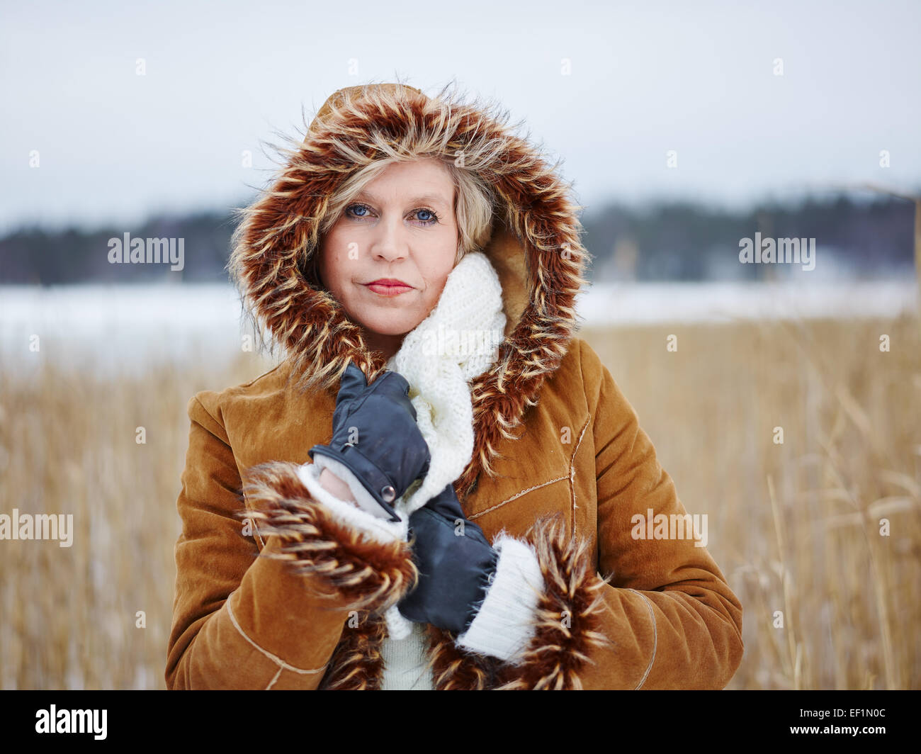 Close up, fashionable mature adult woman wearing winter clothes, frozen sea and reeds on background Stock Photo