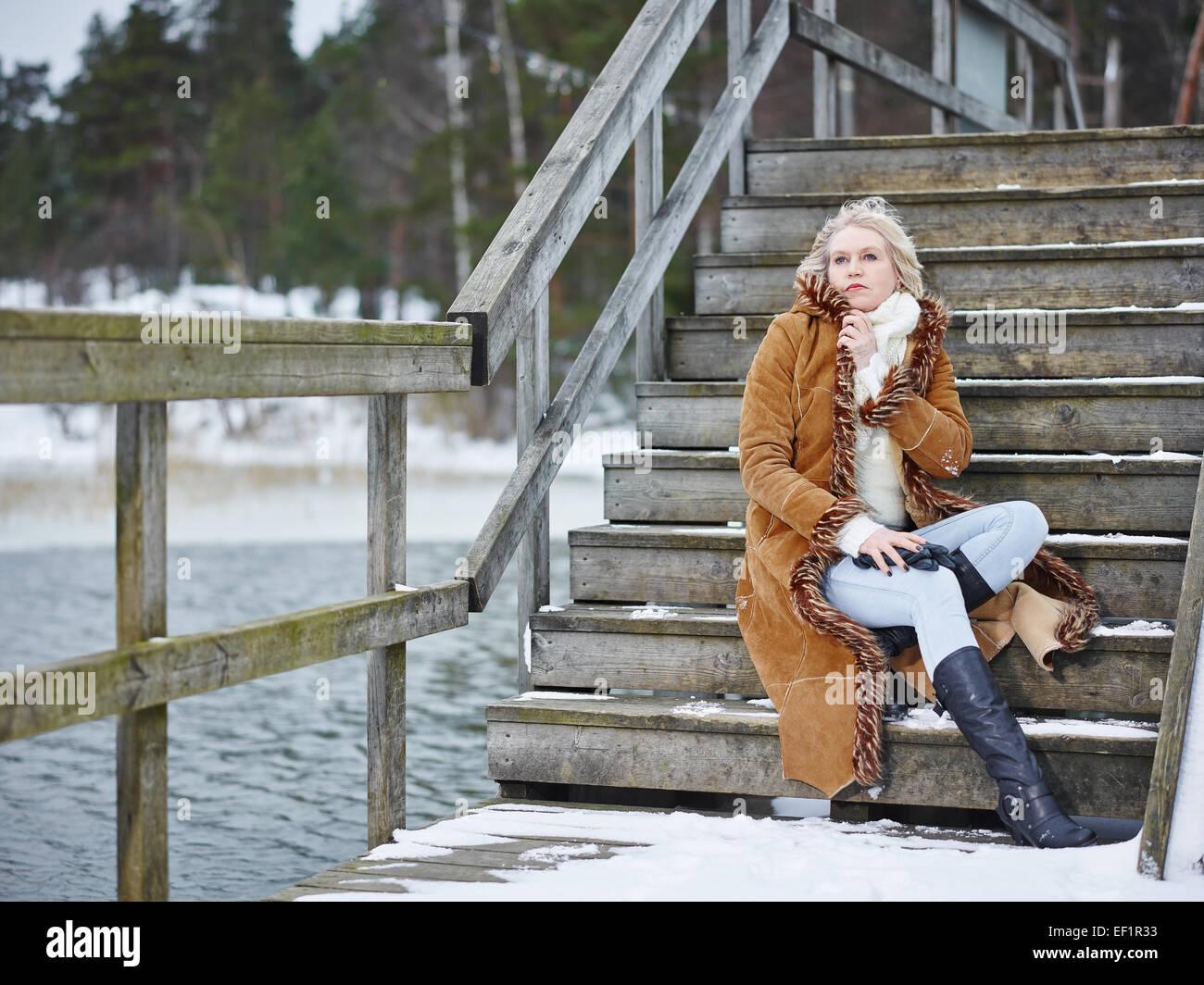 Fashionable mature adult woman wearing winter clothes and she sitting on the stairs - rural scene Stock Photo