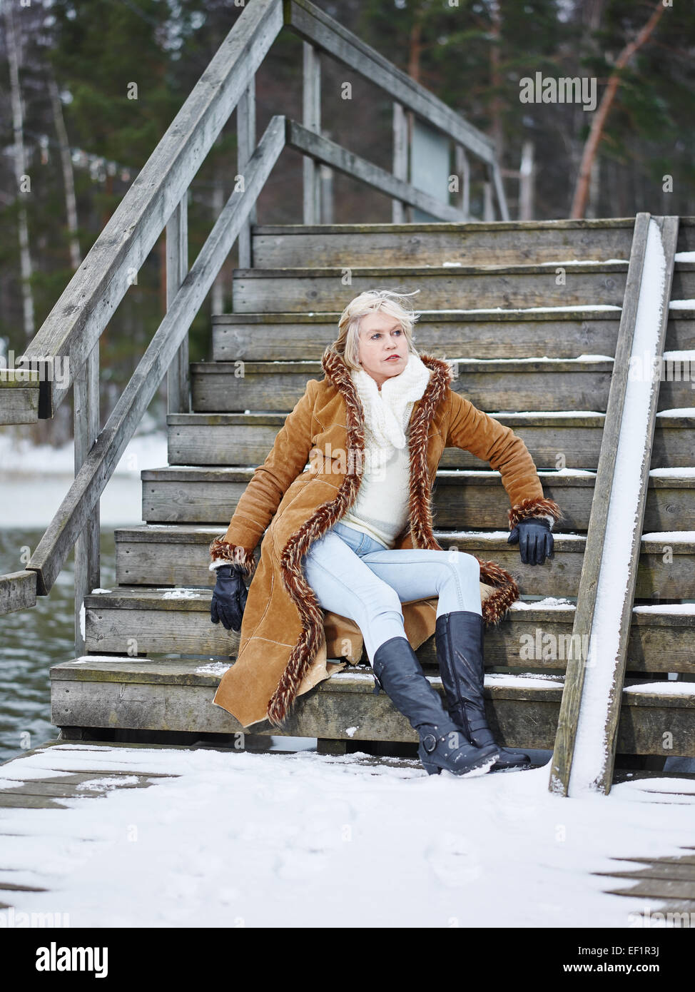 Fashionable mature adult woman wearing winter clothes and she sitting on the stairs - rural scene Stock Photo