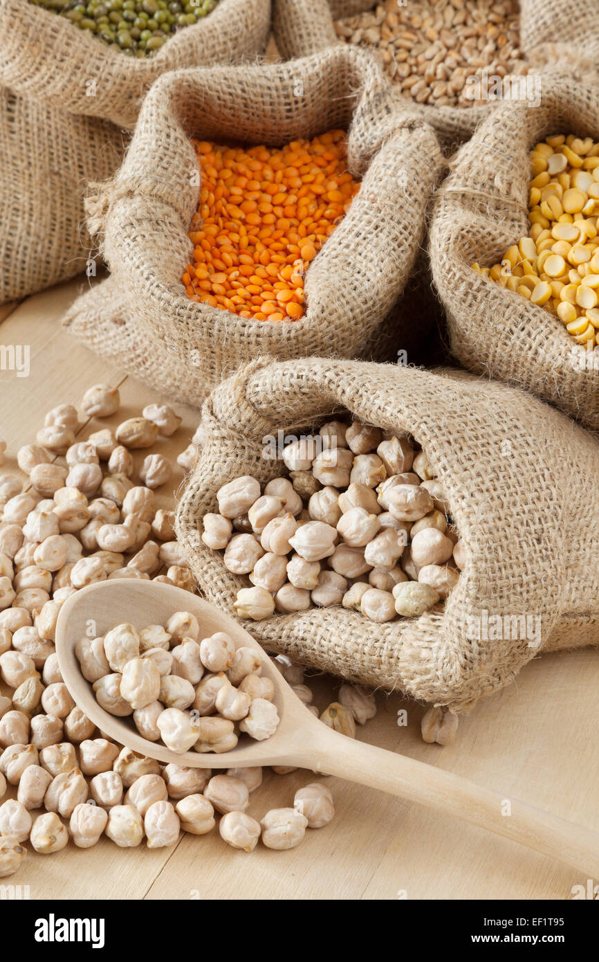 hessian bag with chickpeas and wooden spoon closeup; peas, wheat, red lentils and green mung on background Stock Photo