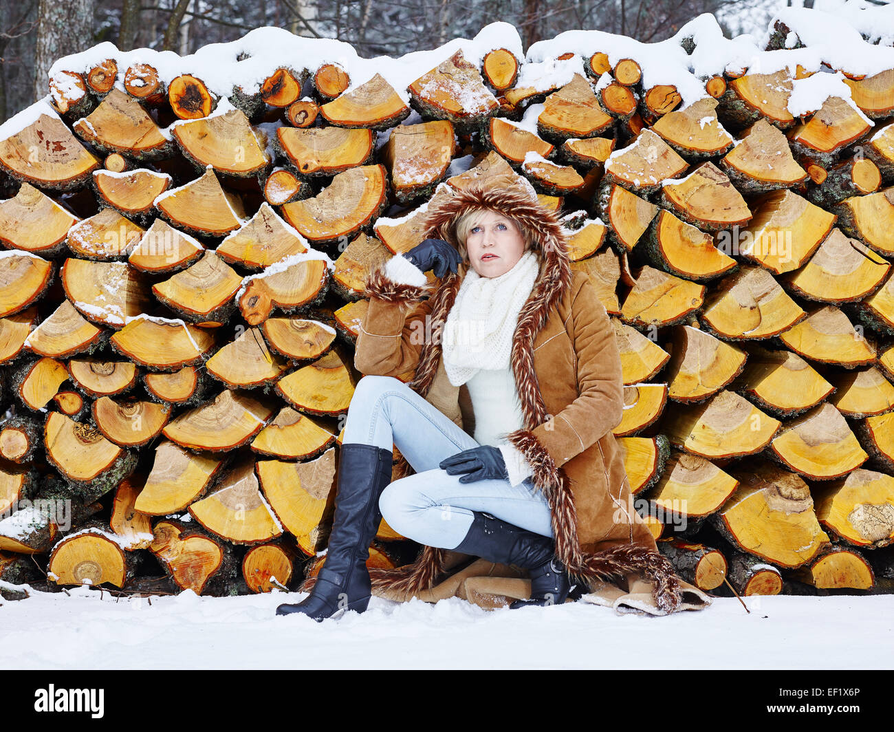 Fashionable mature adult woman wearing winter clothes, rural scene, firewood stack on background Stock Photo