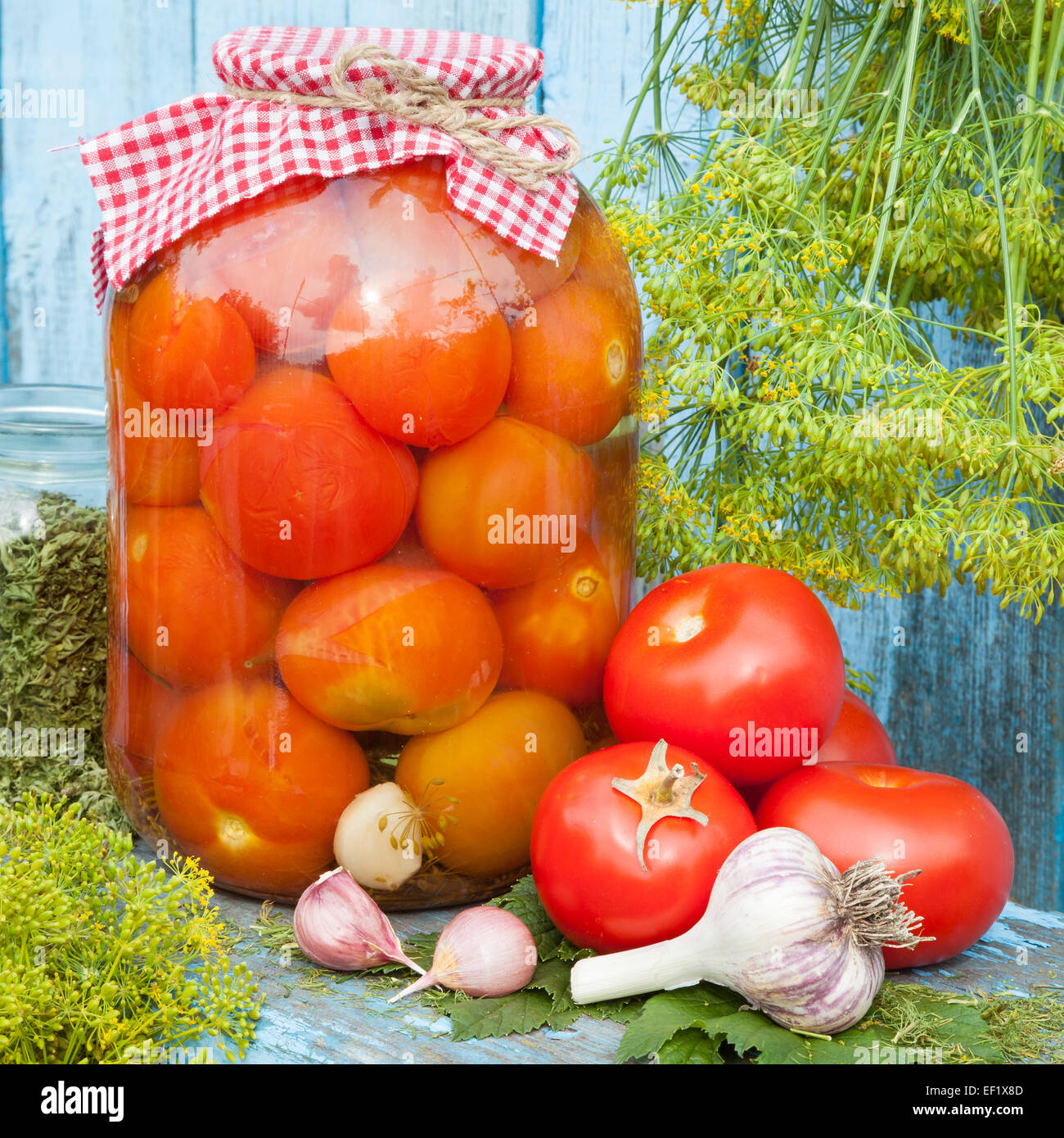 Homemade canned tomatoes in glass jar. Fresh vegetables, dill and garlic on wooden board Stock Photo