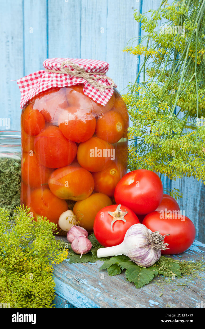 Homemade pickled tomatoes in glass jar. Fresh vegetables, dill and garlic on wooden board Stock Photo