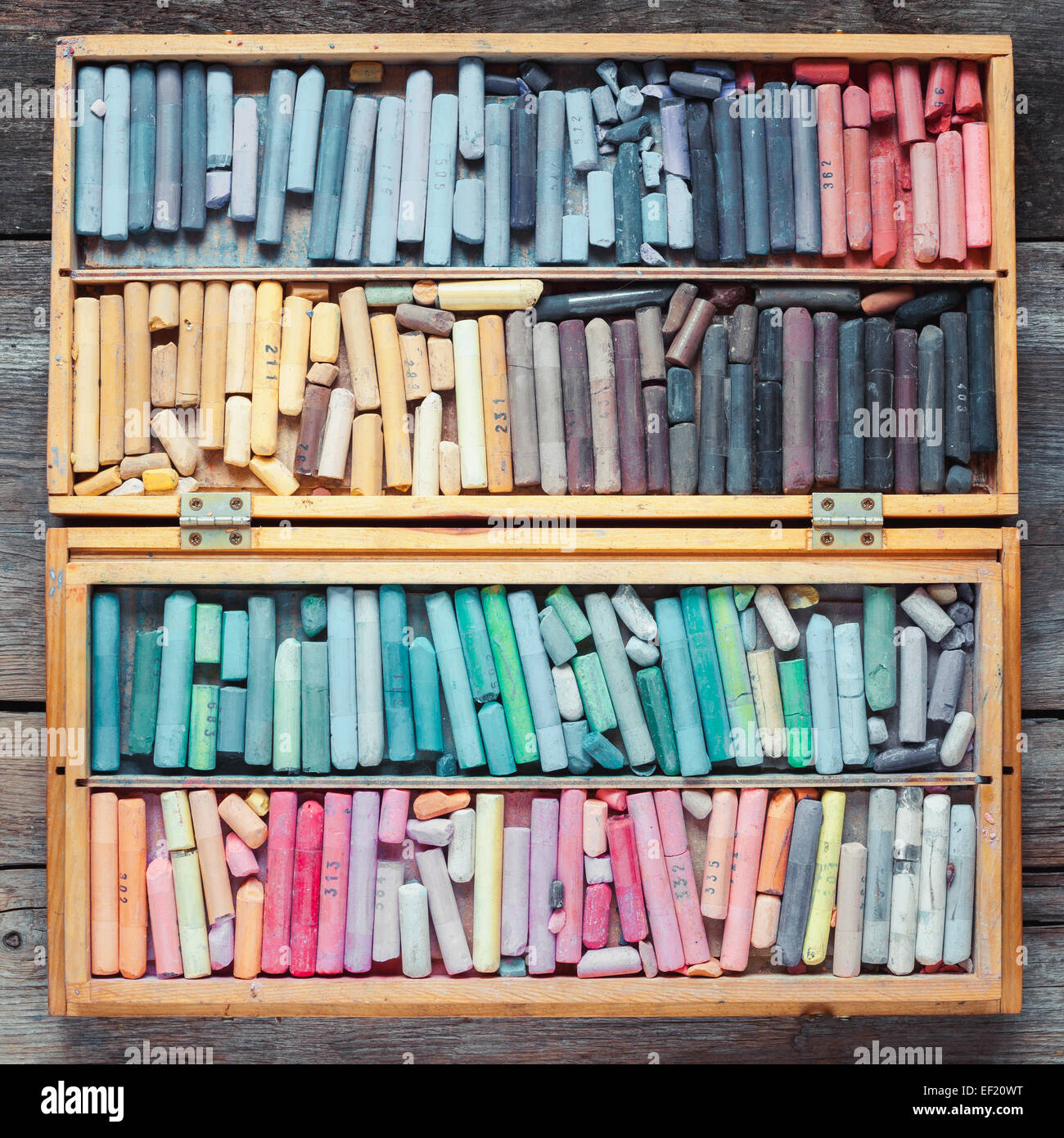 Set of multicolored pastel crayons in open wooden artist box on table