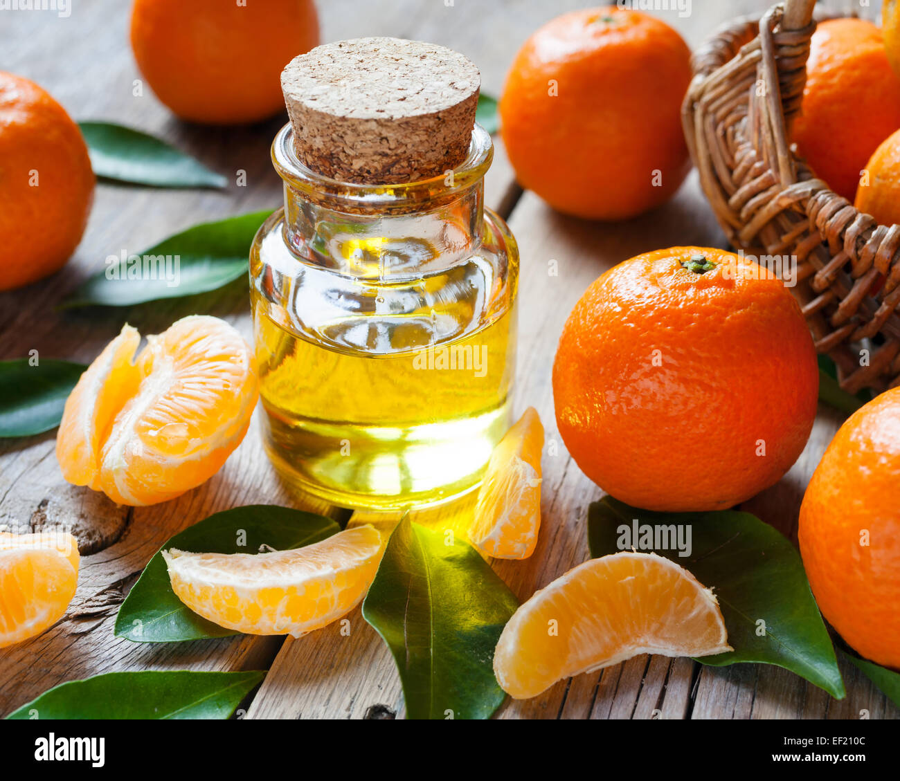 Bottle of essential citrus oil and ripe tangerines with leaves on old wooden kitchen table. Stock Photo