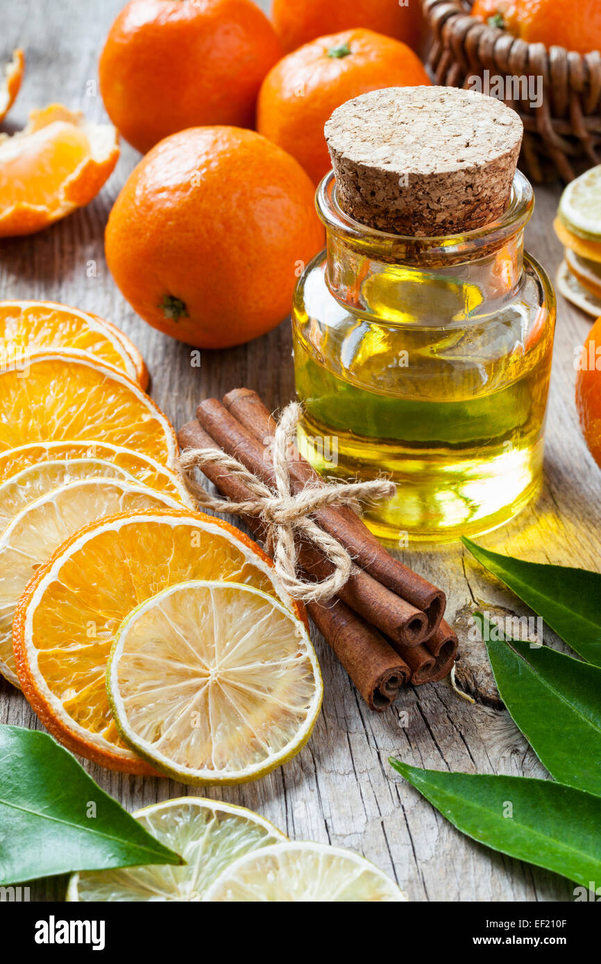 Bottle of essential citrus oil, dried orange and lemon slices, cinnamon sticks and ripe tangerines on old table. Stock Photo